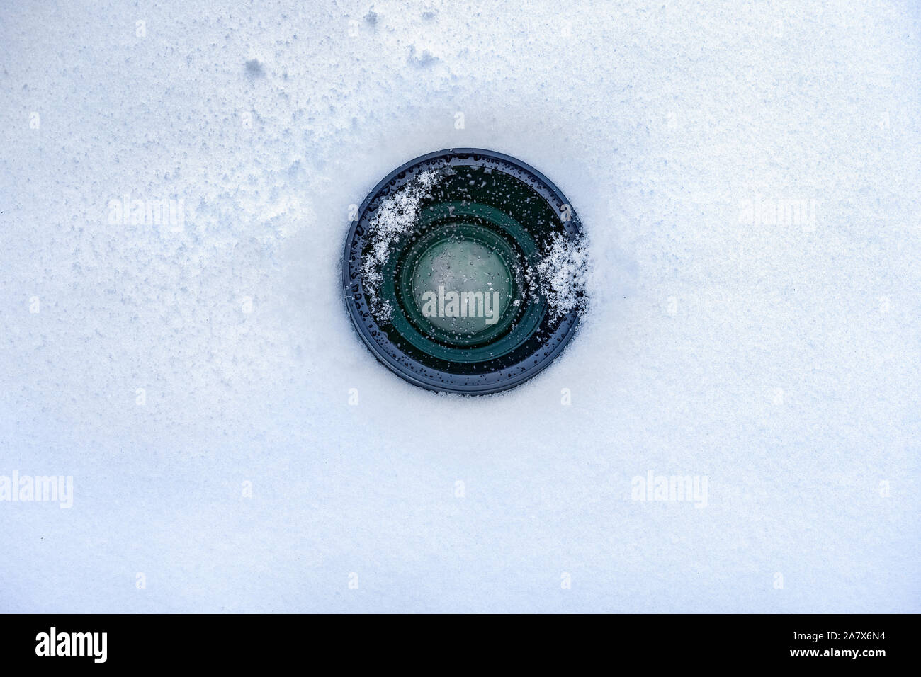 Espionage background. Hidden camera lens in the snow. Black lens of the secret camera is hidden in the snow. Copy space Stock Photo
