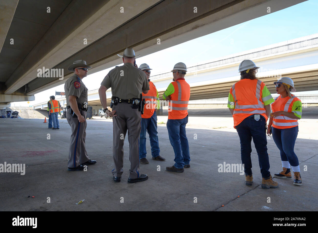 Texas state trooper oversee highway department workers hired to clean up a homeless camp in the public right-of-way under a highway overpass in Austin, Texas. Texas Gov. Greg Abbott ordered the removal of the encampments at 17 sites around the city. Stock Photo