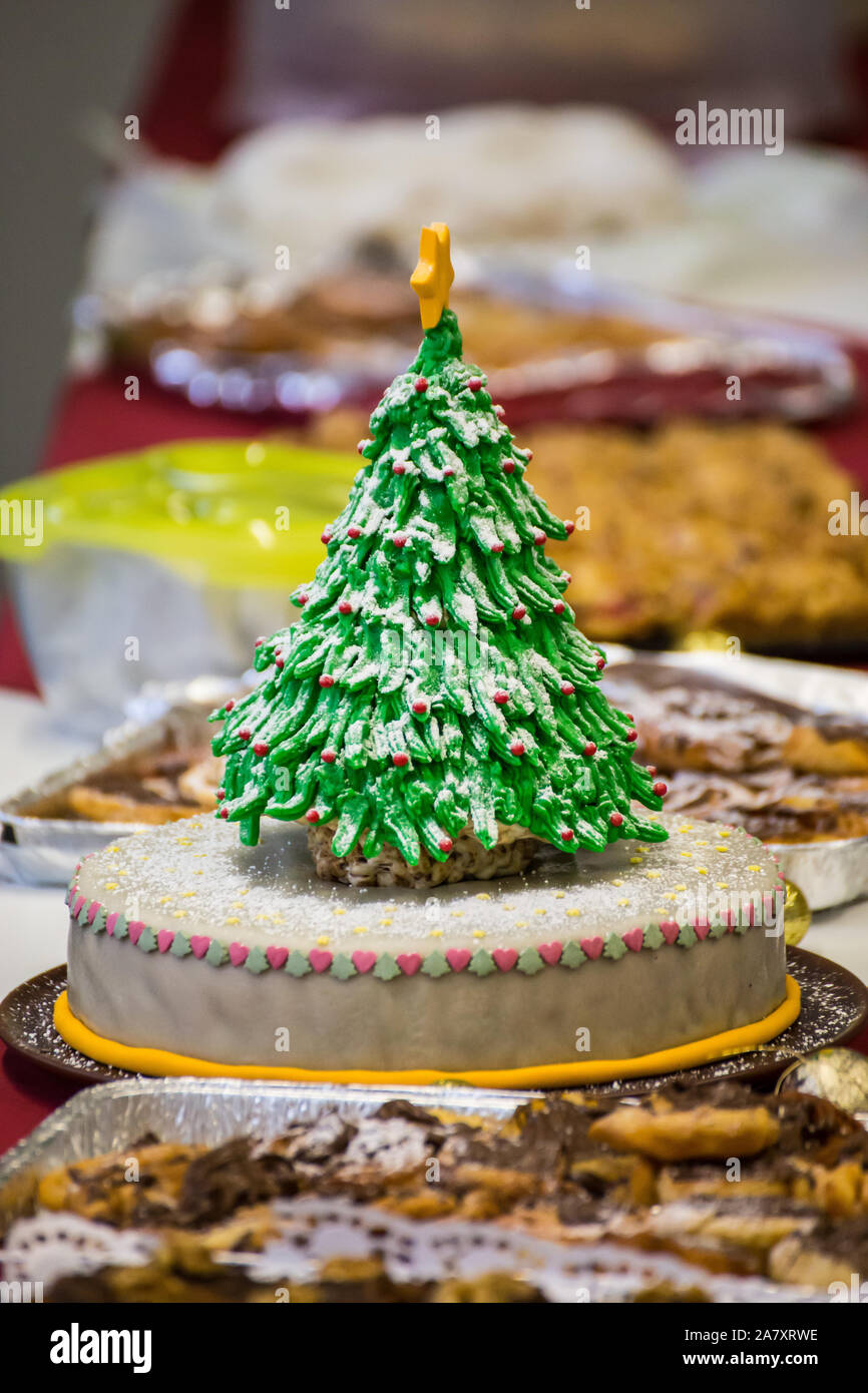 Simple cake dekorated with an eatable christmas tree pops out amonst other pies and cakes on a christmas party. Stock Photo
