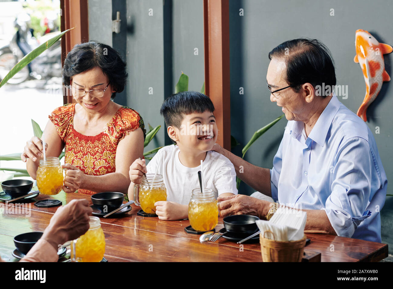 Happy little Vietnamese boy enjoying spending time with grandparents in cafe Stock Photo