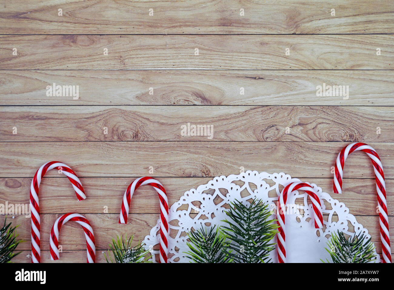 Seasonal Christmas flat lay with white lace doily, candy canes and fir branches with snow on wooden copy space background Stock Photo