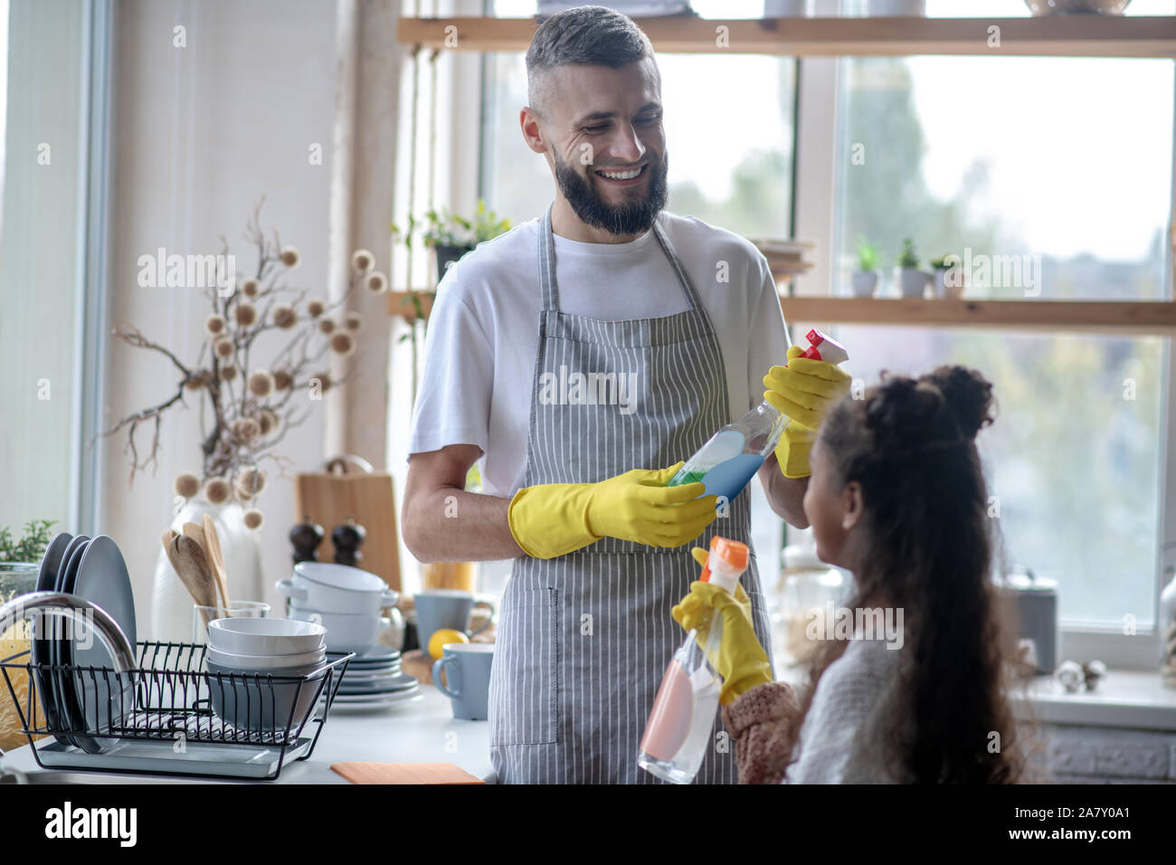 Beaming father taking detergents while cleaning kitchen with daughter ...