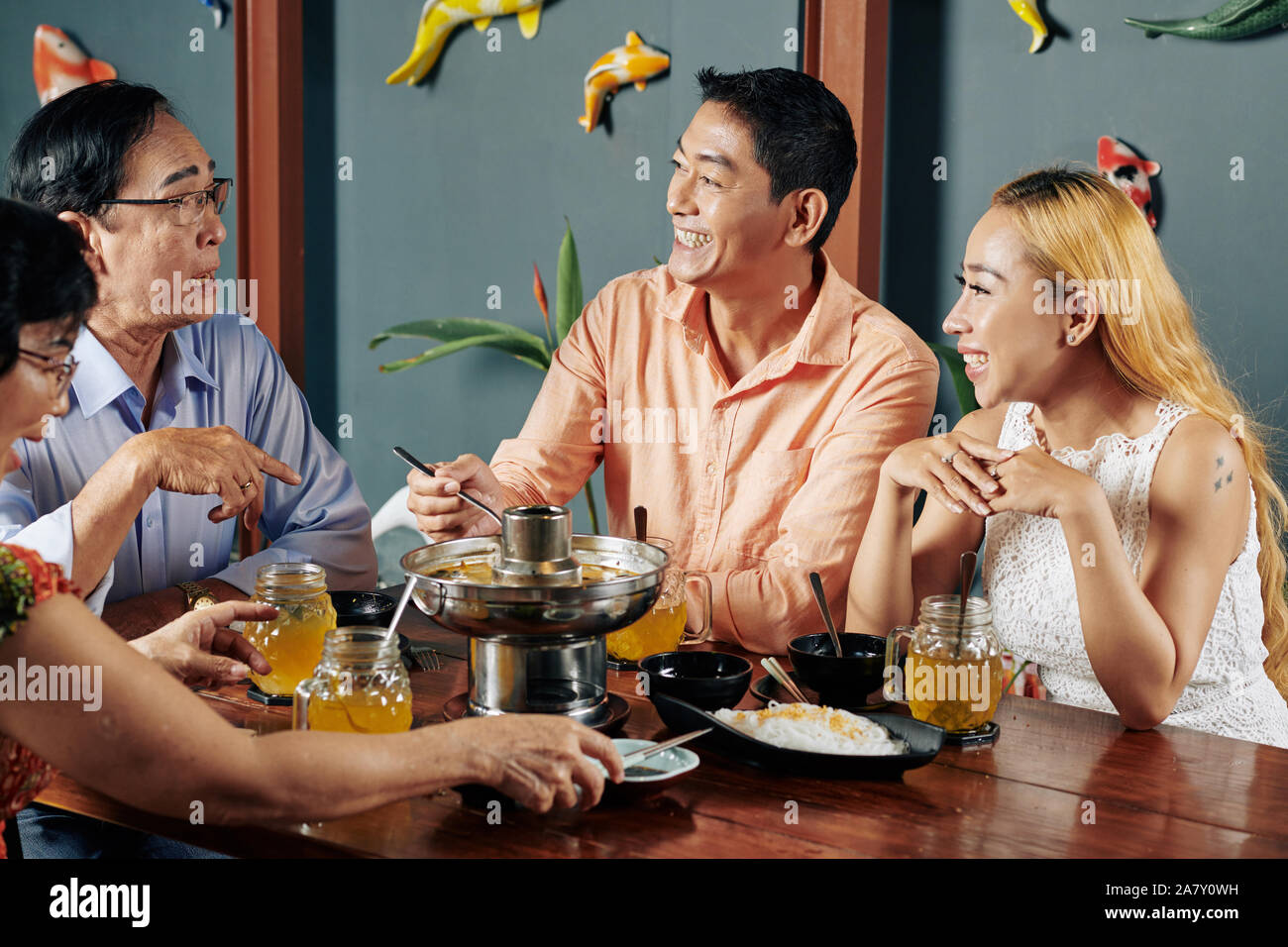 Cheerful mature couple and their senior parents talking and joking when having dinner at home together Stock Photo