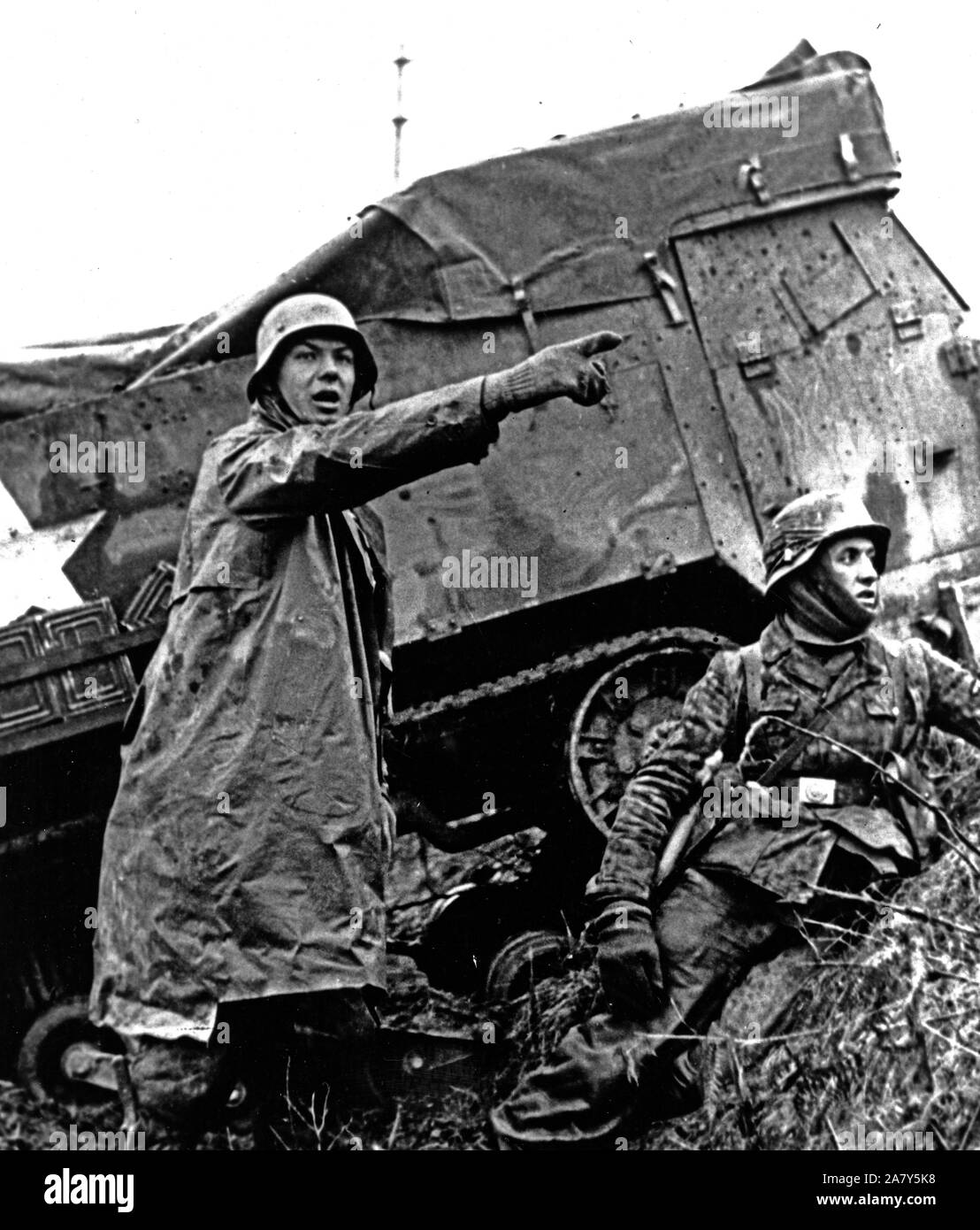 This photo from a captured German film shows a Nazi soldier beside a disabled American half-track signaling his unit to advance during the counter-attack the Germans launch Stock Photo