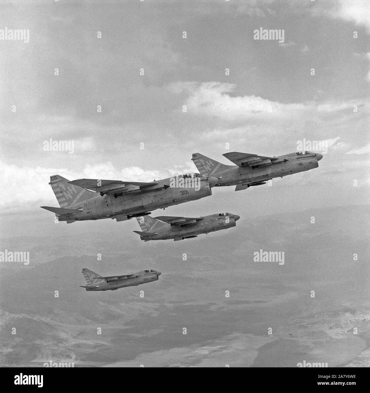 An air-to-air right side view of three A-7E Corsair II aircraft of Attack Squadron 22 (VA-22) carrying AIM-9 Sidewinder missiles and Mark 82 500-pound bombs.  The aircraft are en route to a target range at Naval Weapons Center, China Lake. Stock Photo