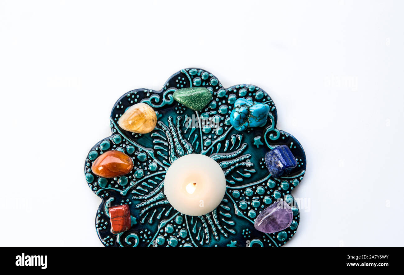 Top view of all 7 chakra colors semi precious crystal stones on blue and white ornament background with relaxing candle burning in center. Lot of copy Stock Photo