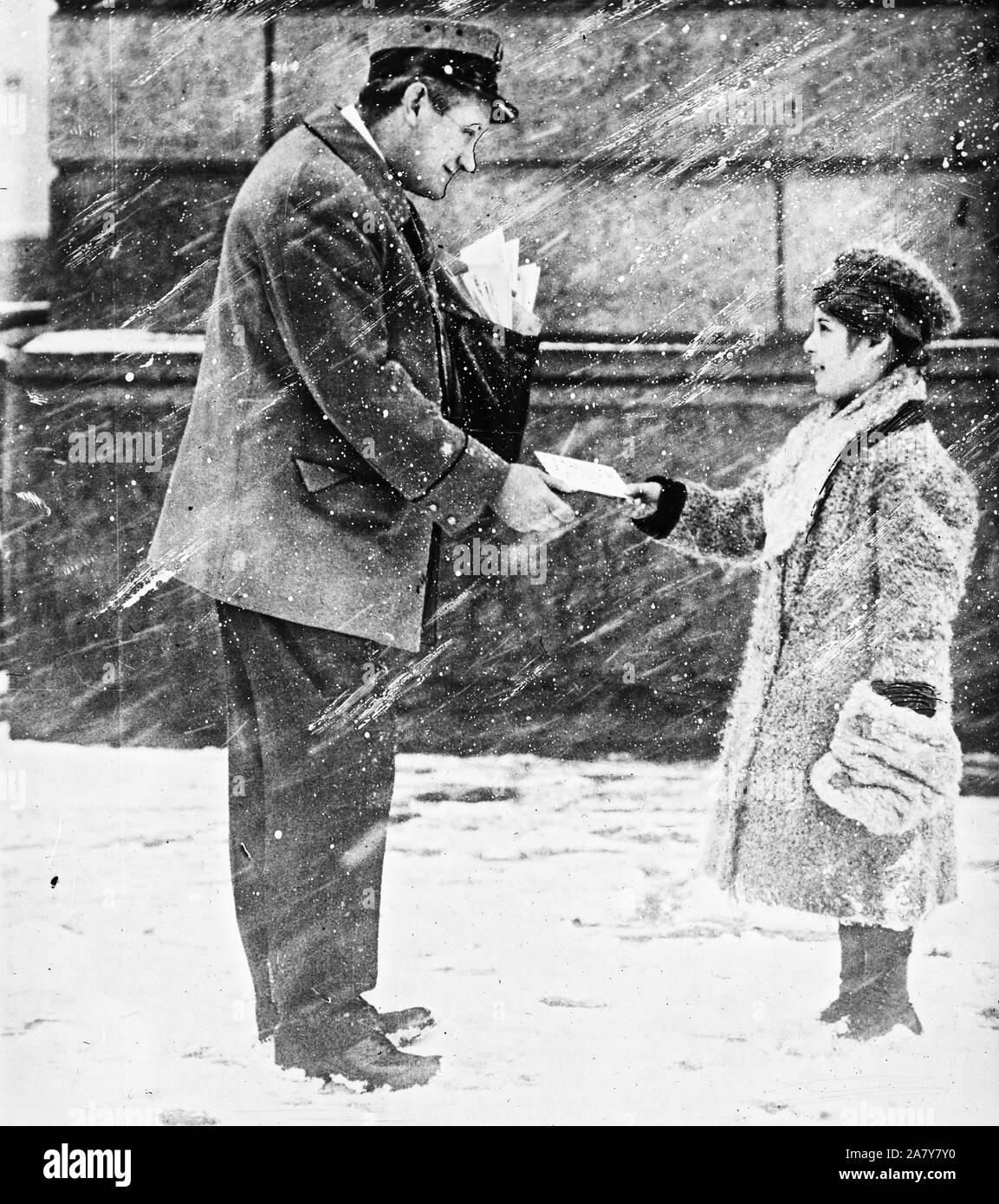 boy giving mailman a letter for Santa Claus in early 1900s, early 20th century while standing in the snow Stock Photo