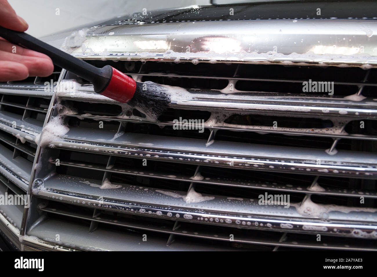 A male worker washes a black car with a special brush for grille and
