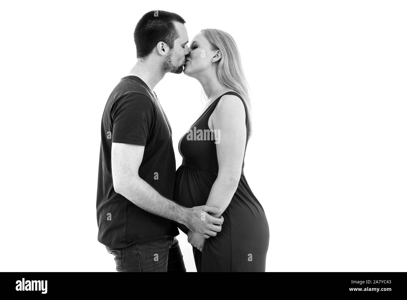 Young pregnant couple in love expecting child, studio portrait. Husband hugging his pregnant wife in intimate relationship. Young pregnant couple kiss Stock Photo