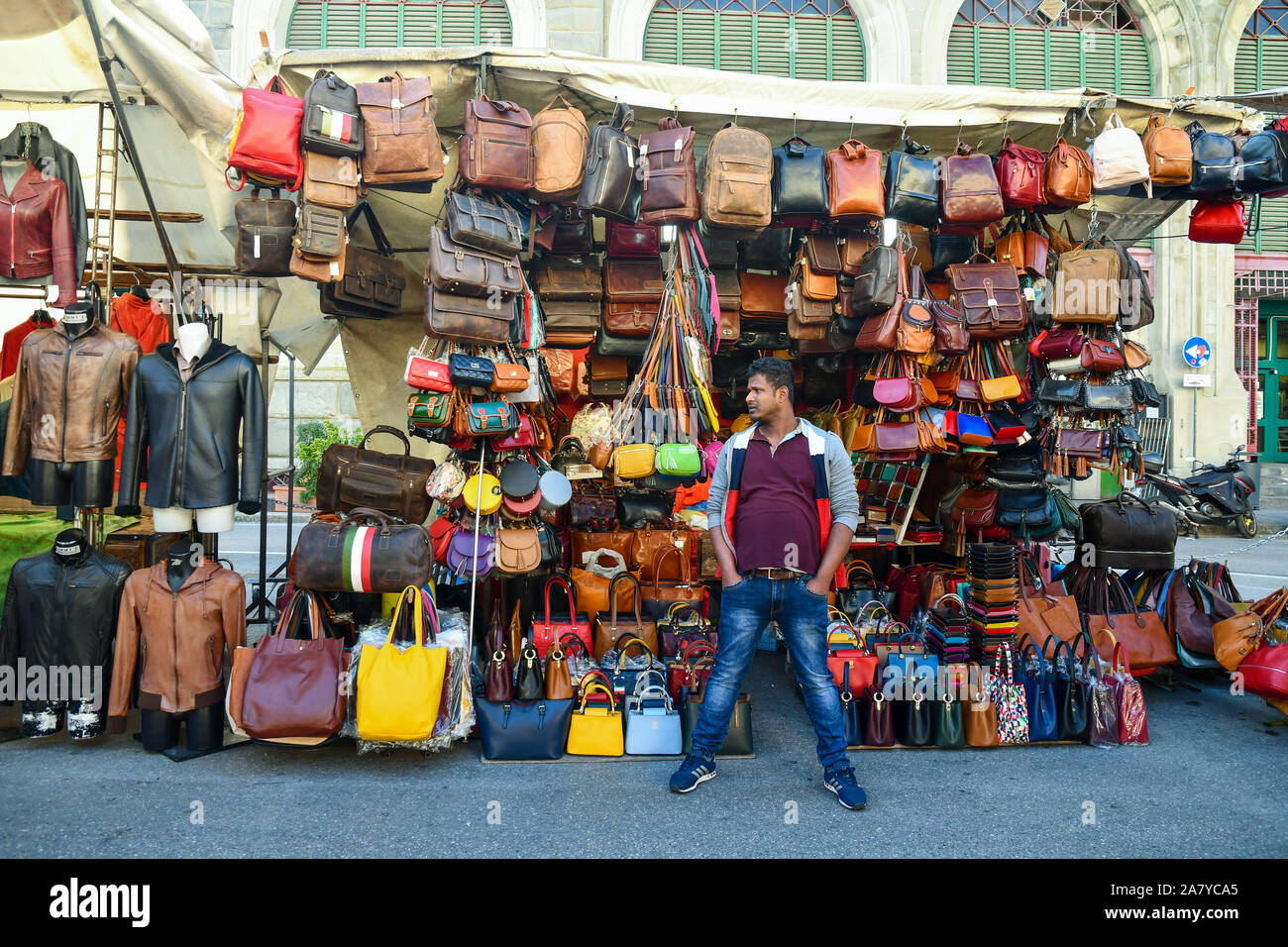 A foreign peddler in front of his stall of leather goods in St Lawrence Central Market square in the city center of Florence, Tuscany, Italy Stock Photo