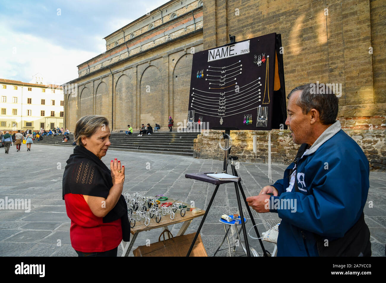 A lady bargaining the price of a necklace with a peddler in front of the Basilica of San Lorenzo in the city center of Florence, Tuscany, Italy Stock Photo