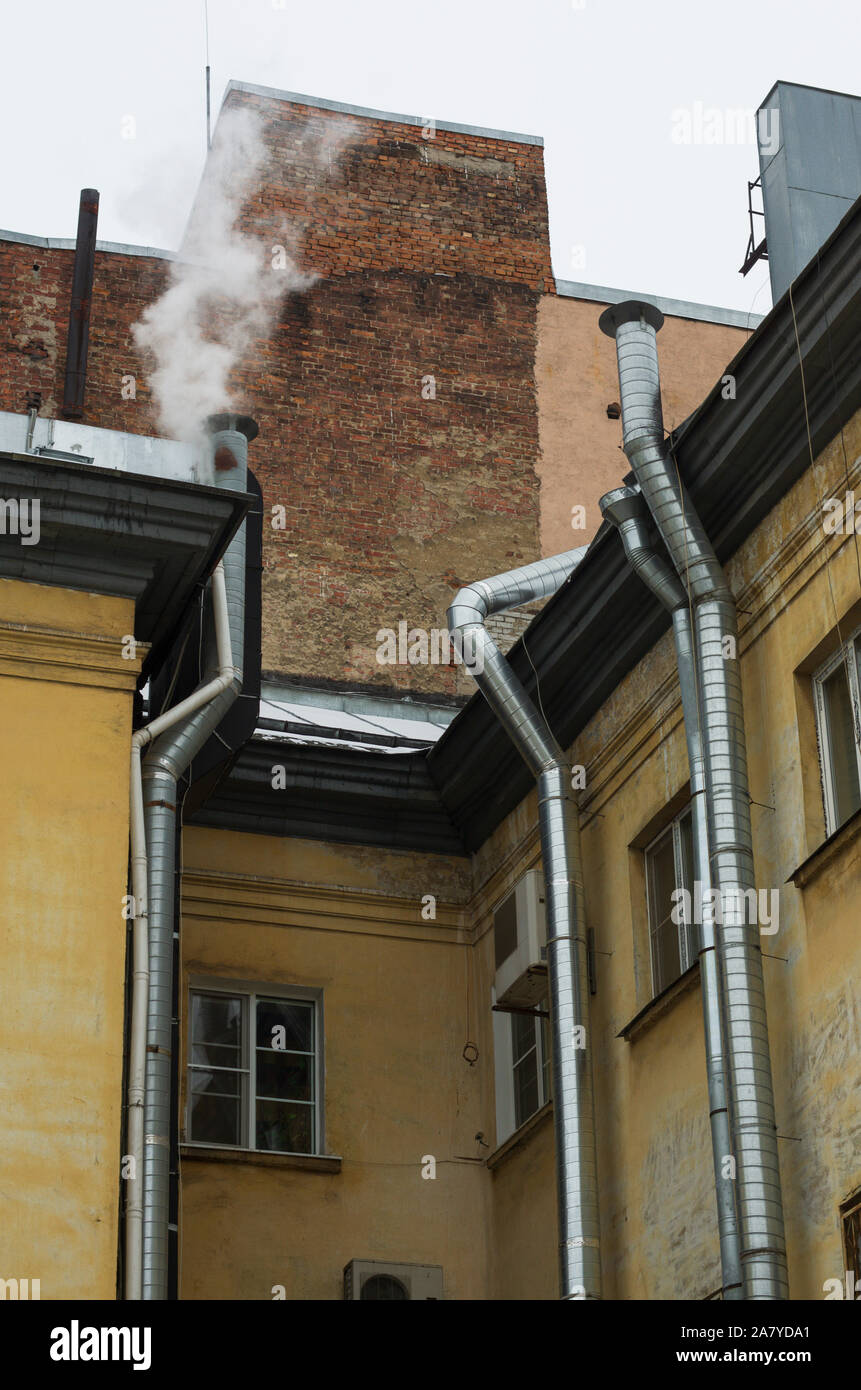 Walls of old houses with silvery pipes ventilation system with smoke over one of the pipes