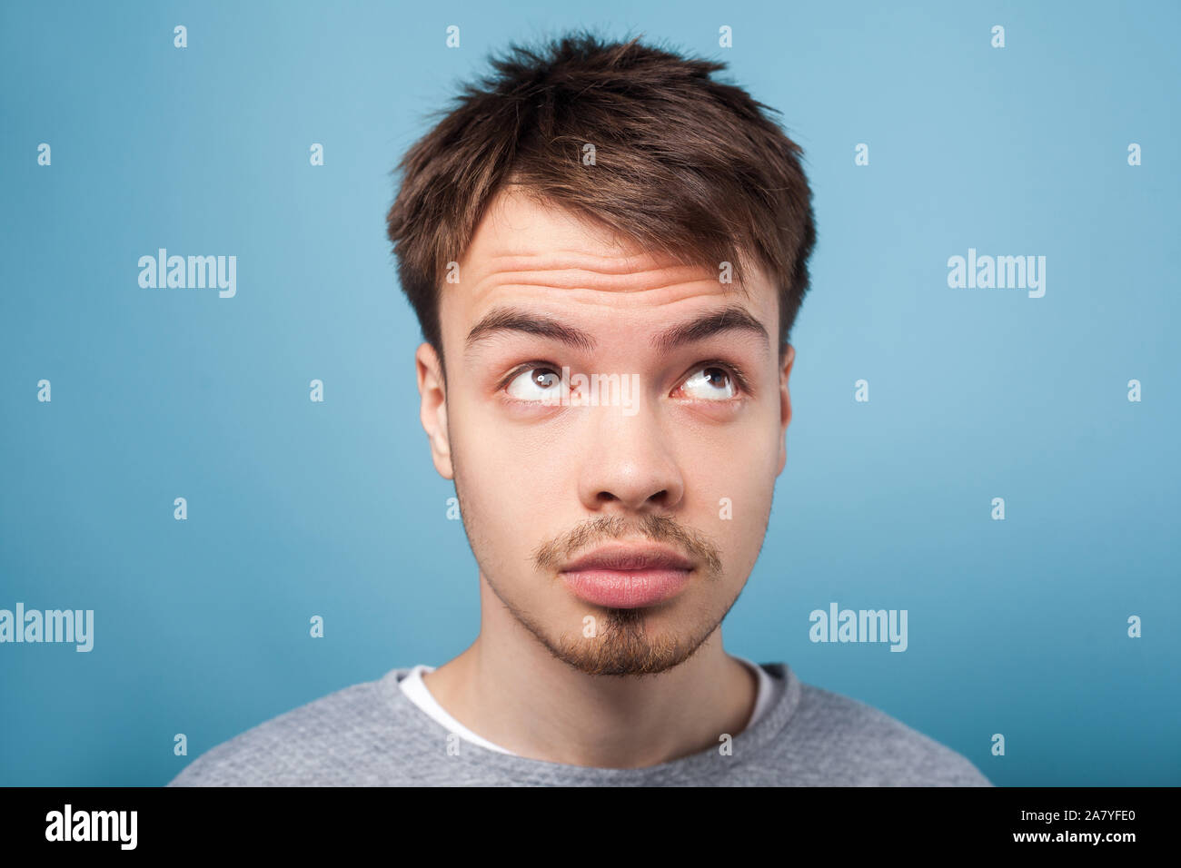 What's with my hair. Closeup portrait of young brunette man with small beard and mustache in casual sweater looking up with inquiring gaze, dissatisfi Stock Photo