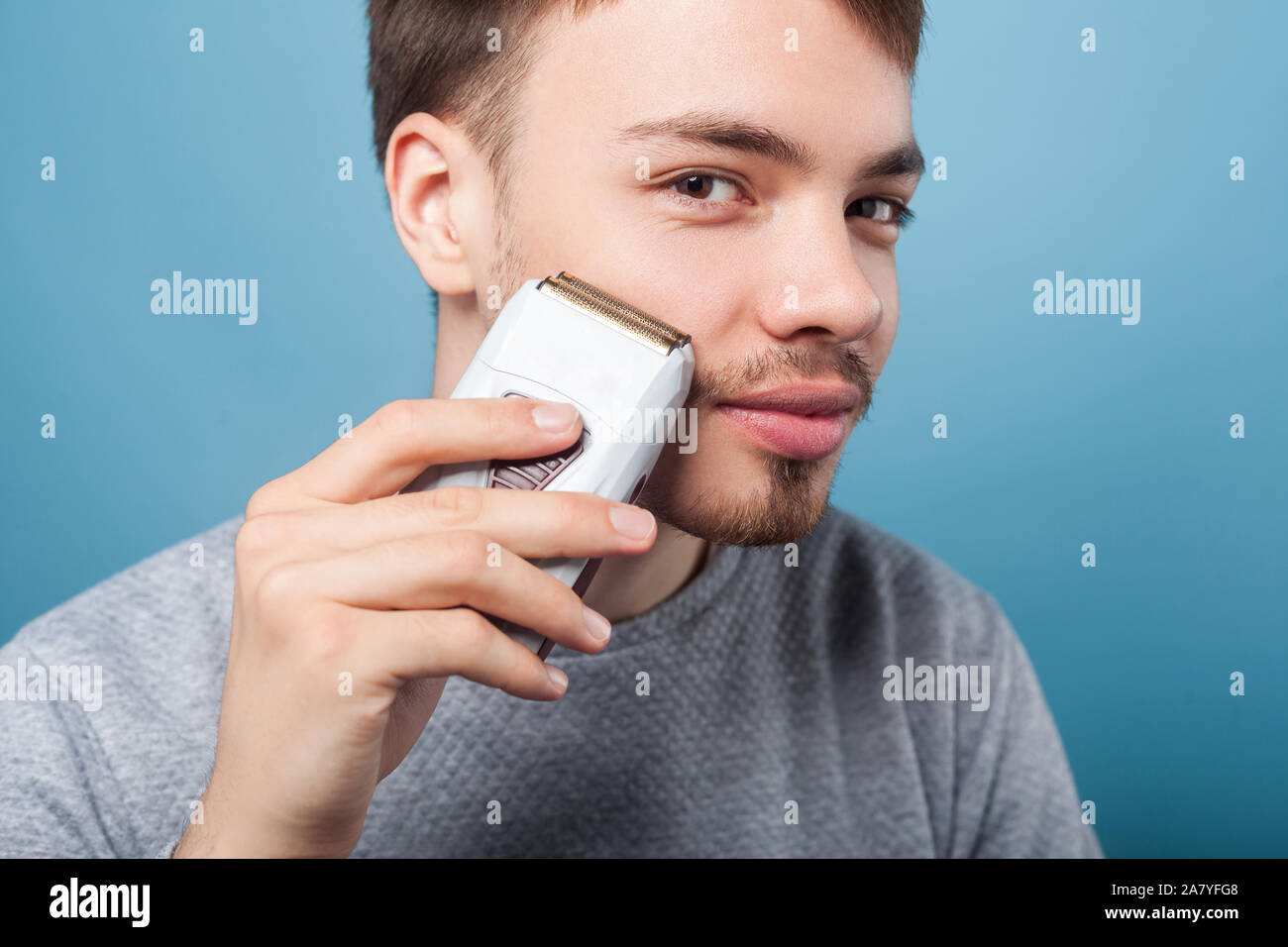 Portrait of happy brunette man with bristle and mustache using epilator to remove facial hair, smiling satisfied with soft skin, male beauty care conc Stock Photo