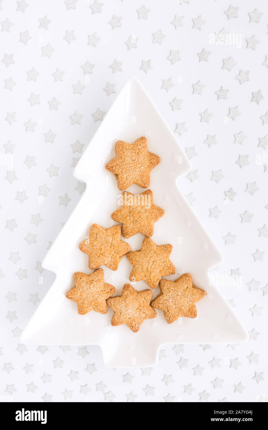 Star shaped homemade Christmas biscuits on tree shaped plate and silver star confetti on white background with copy space. Top view. Stock Photo