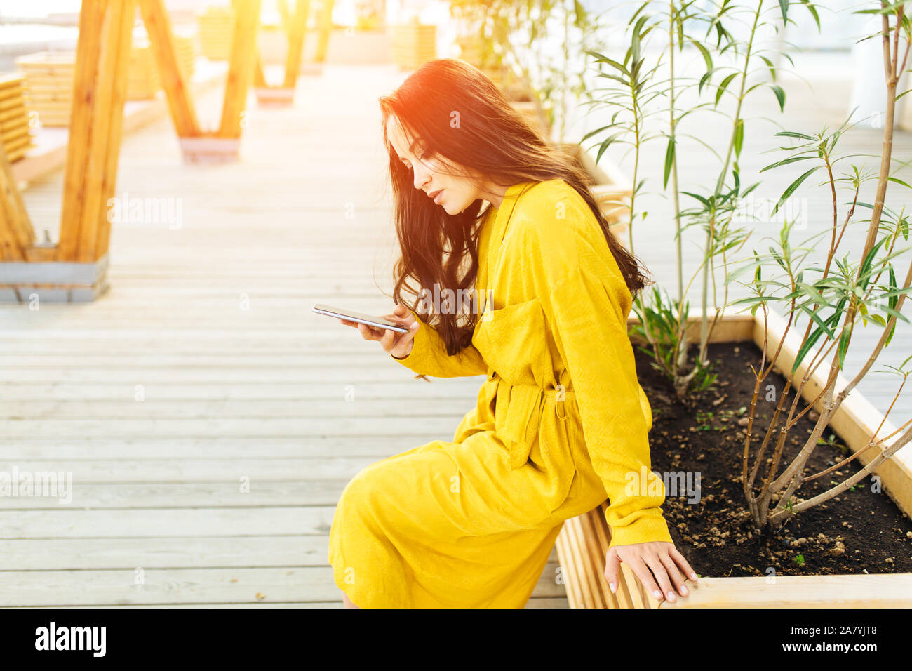 Happy girl using a smart phone in a city park sitting in yellow dress ...