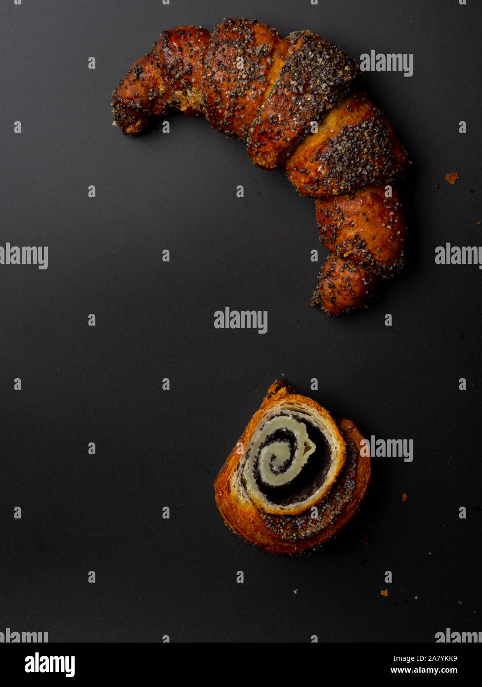 Sweet bun with poppy seeds on black background. Homemade roll horn with