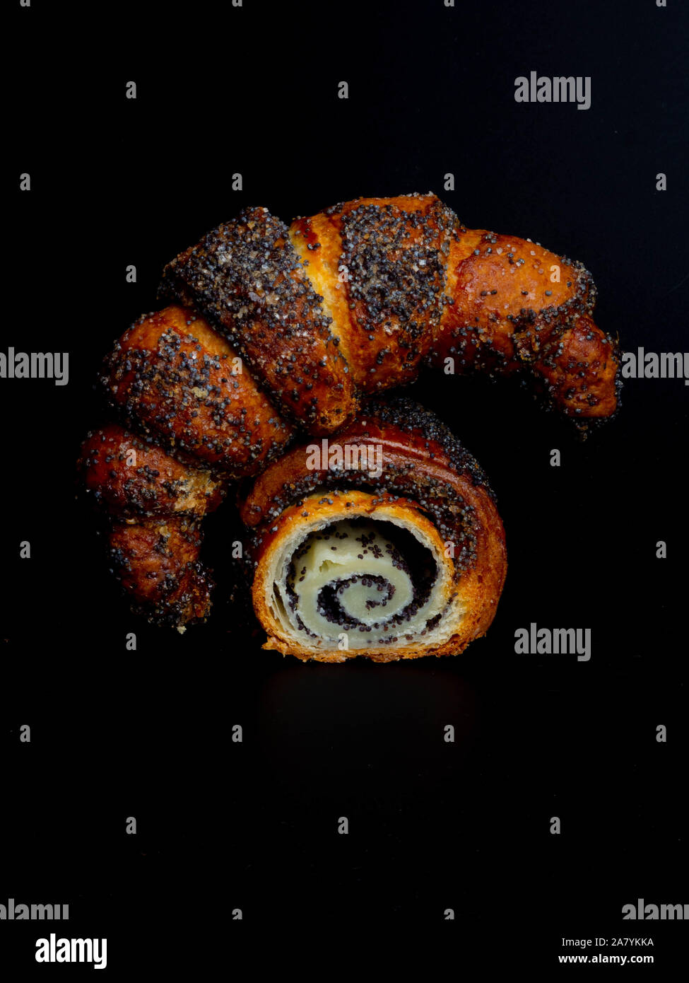 Sweet bun with poppy seeds on black background. Homemade roll horn with