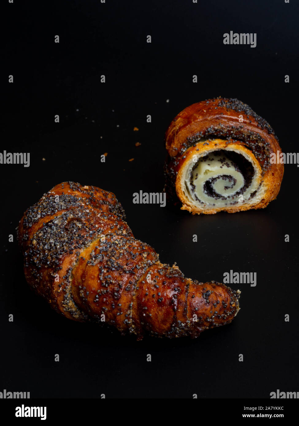 Sweet bun with poppy seeds on black background. Homemade roll horn with