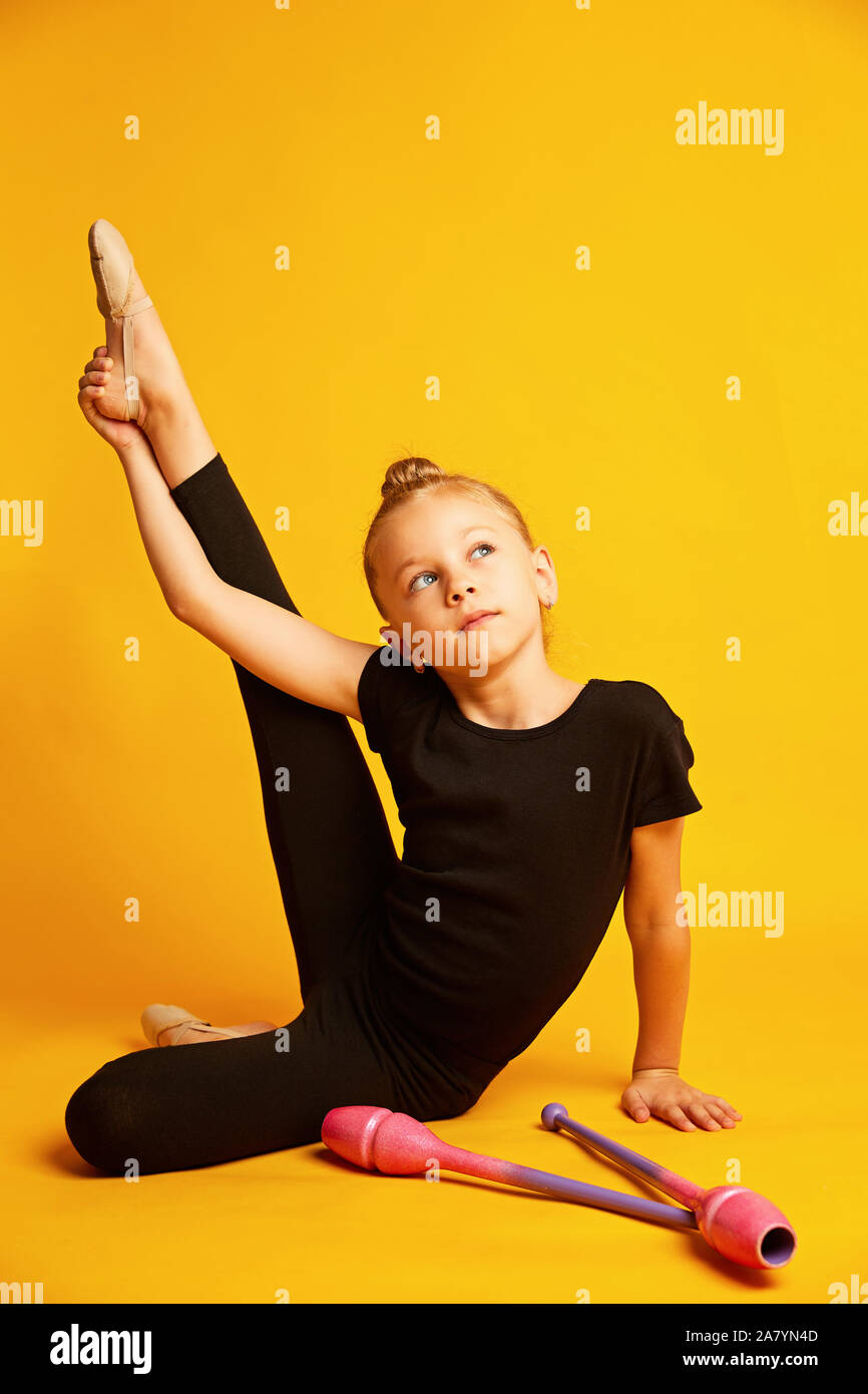 Little gymnast stretching leg near wands during training Stock Photo