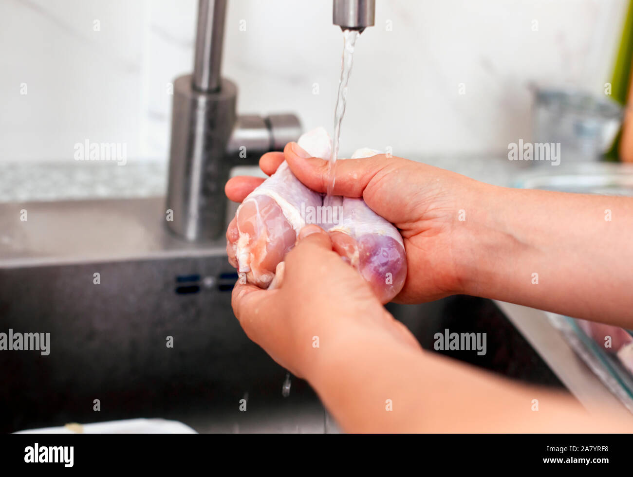Woman hands washing chicken legs in kitchen sink. Closeup Stock Photo