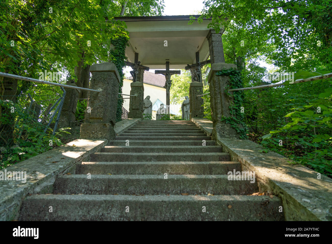 Staircase in the middle of nature area, leading to a Christian sanctuary with three sculptures of Jesus Christ crucified, in Kapuzinerberg hill. Salzb Stock Photo