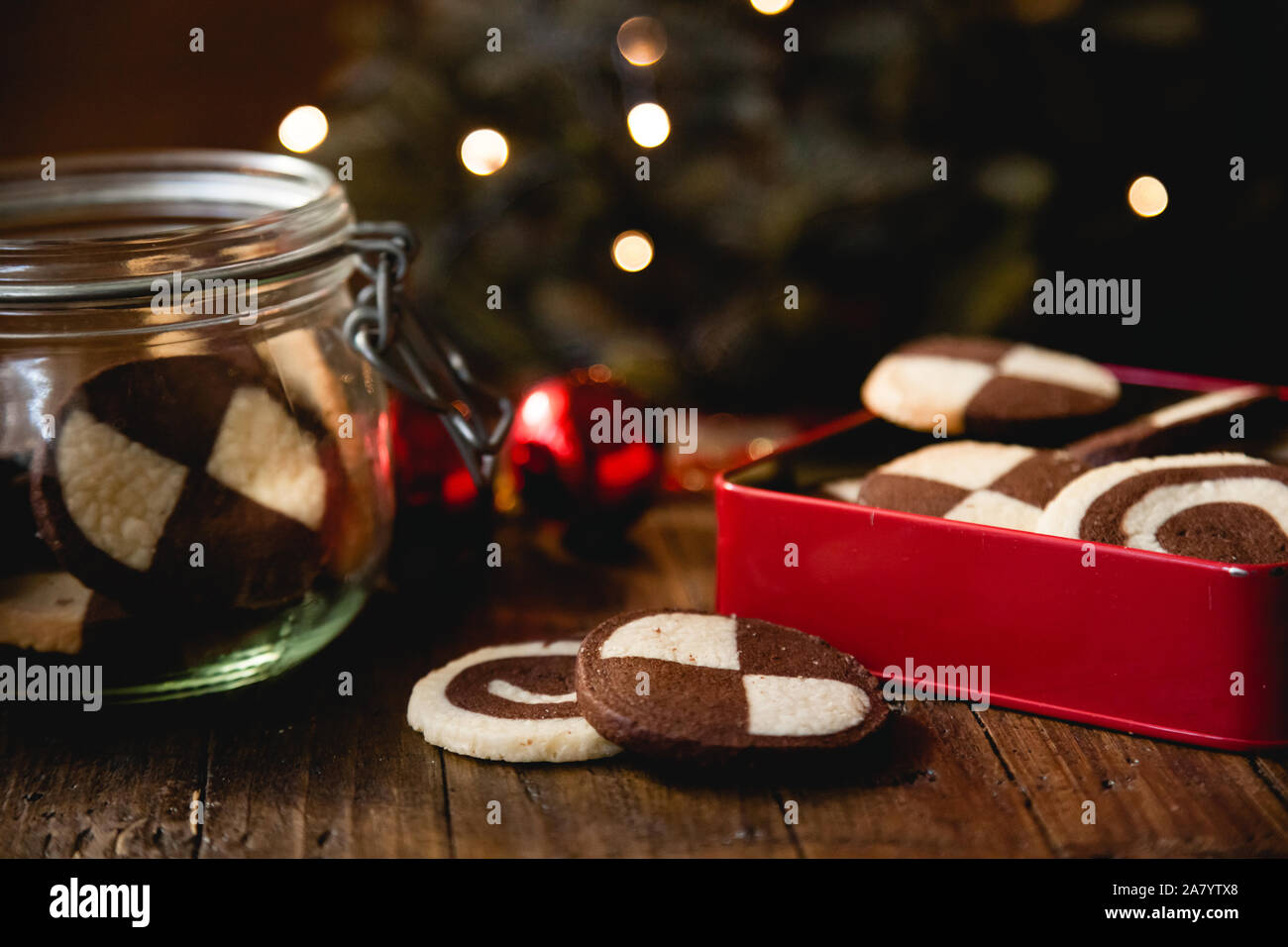 Traditional German Christmas cookies (checkered biscuits) in red biscuit tin on wooden table with christmas decoration and lights in the background Stock Photo
