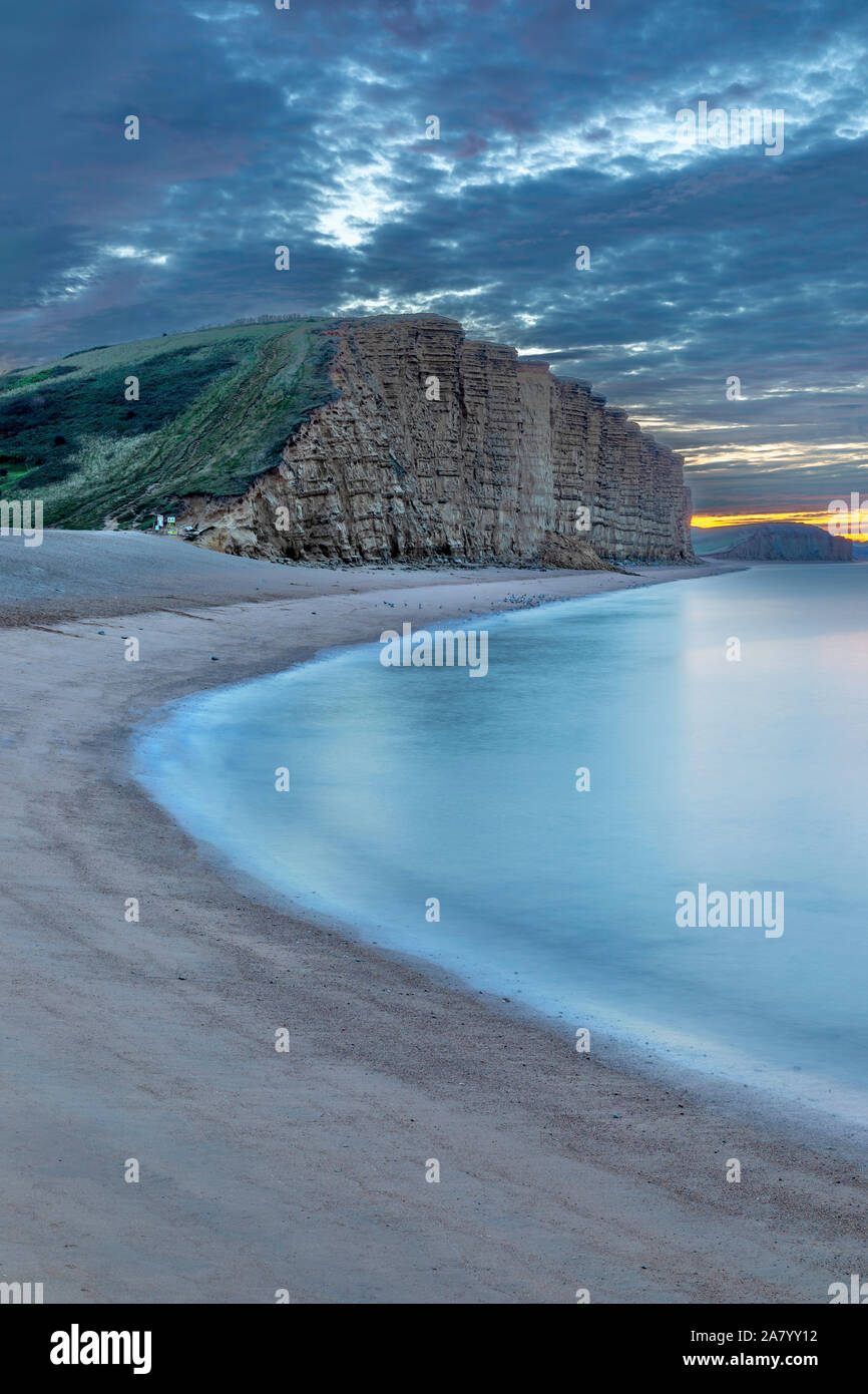 West Bay Dorset England The near vertical cliffs of Dorset's Jurassic coast seen at West Bay, the port for Bridport, at sunrise. Stock Photo