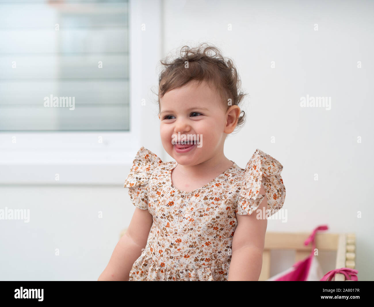 1 year old baby girl stands in her cot (or crib) Stock Photo