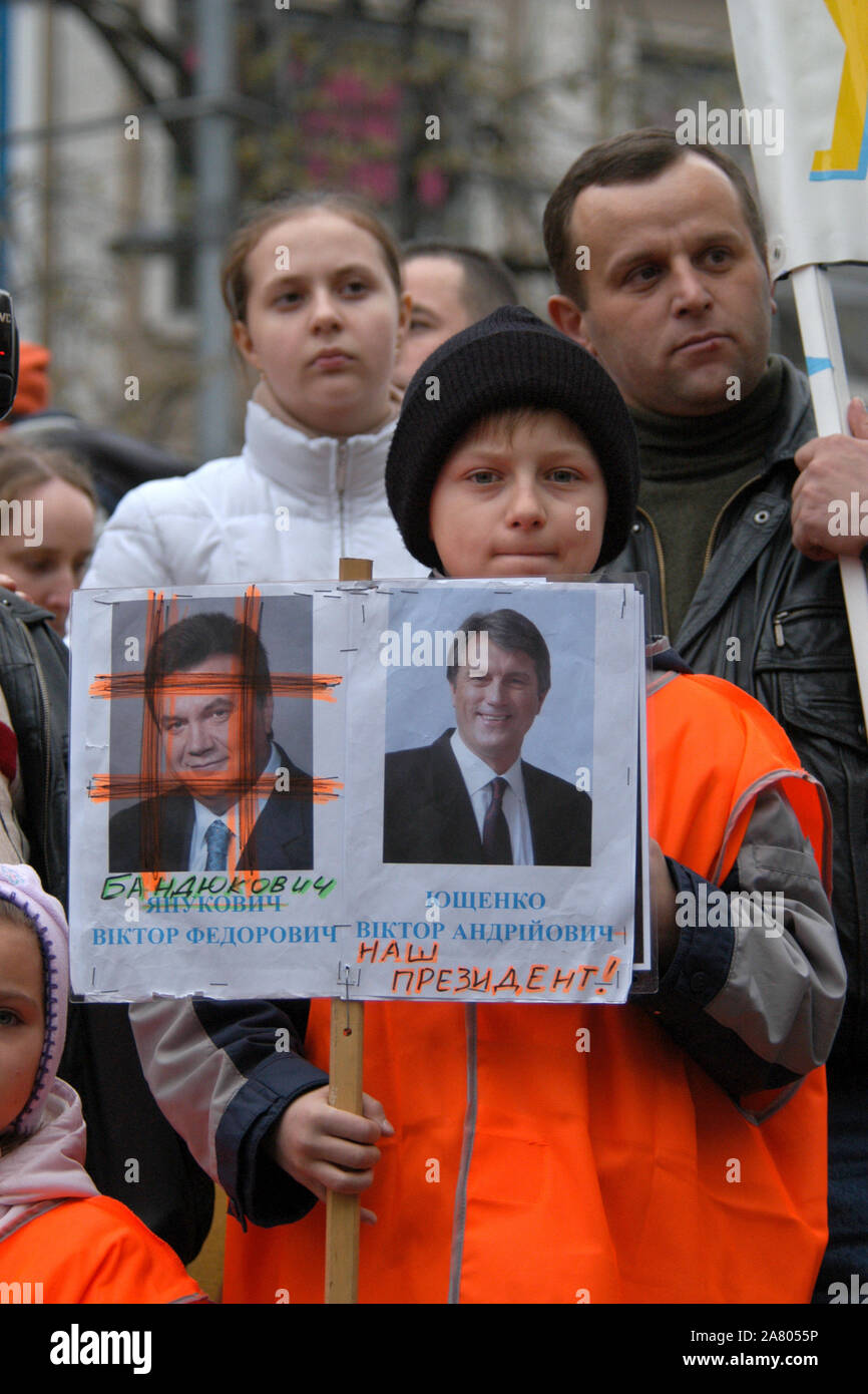 Orange revolution in Ukraine. Young boy dressed orange attends the demonstration of Ukrainian migrants in the Czech Republic to support Ukrainian oppositional presidential candidate Viktor Yushchenko in Wenceslas Square in Prague, Czech Republic, on November 28, 2004. The inscription under the portrait of presidential candidate Viktor Yanukovych (L) is changed to Bandukovych (literally a bandit or a robber). The inscription under the portrait of presidential candidate Viktor Yushchenko (R) is added with words 'Our President'. Stock Photo