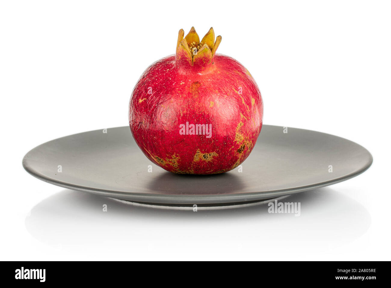 One whole fresh red pomegranate on gray ceramic plate isolated on white background Stock Photo
