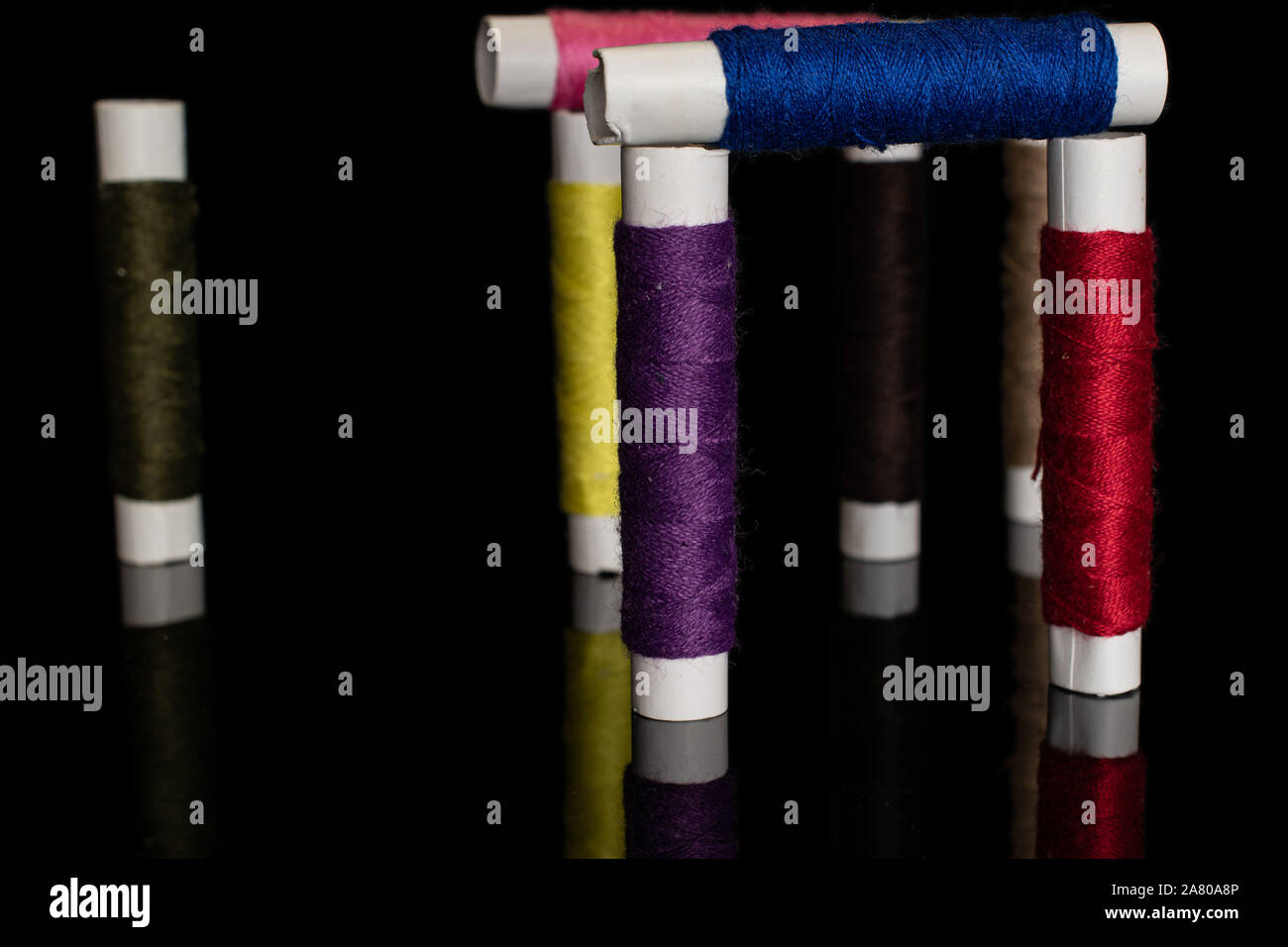 Group of eight whole colorful sewing thread spool isolated on black glass Stock Photo