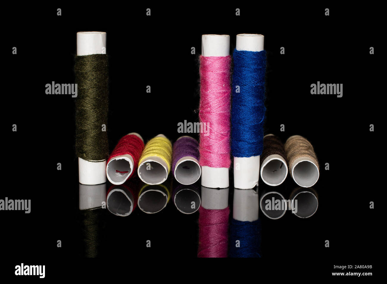 Group of eight whole colorful sewing thread spool upright isolated on black glass Stock Photo