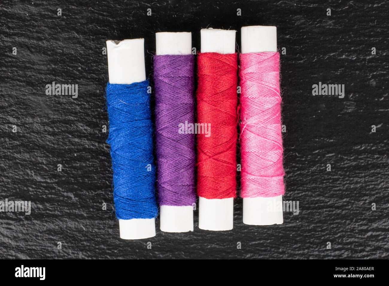 Group of four whole sewing thread spool in row flatlay on grey stone ...