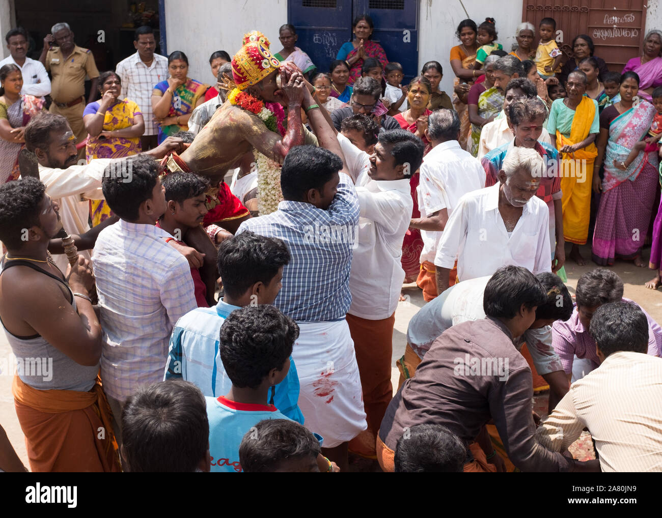 Priest on shoulders of devotees drinking the blood of a sacrificed young goat during Kutti Kudithal Festival in Trichy, Tamil Nadu, India Stock Photo