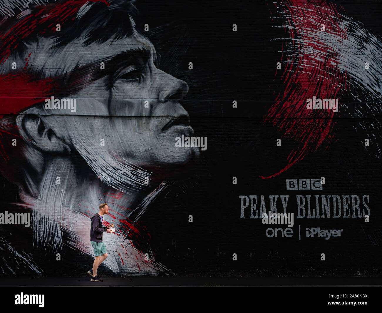 Man walking and eating in front of Peaky Blinders artistic graffiti on wall in london Stock Photo