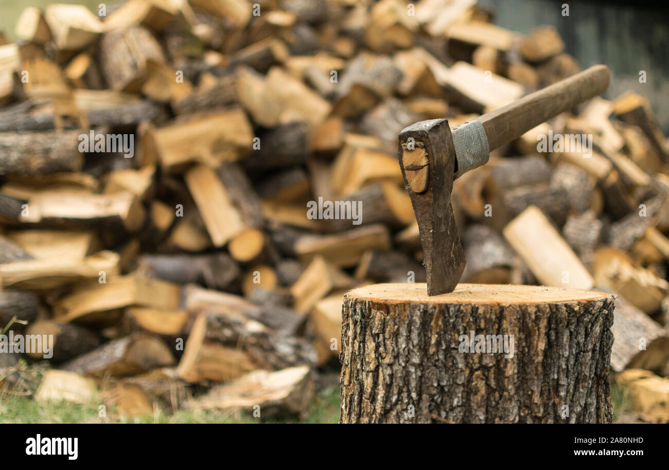 An axe stuck in a log in front of a pile of wood. Stock Photo