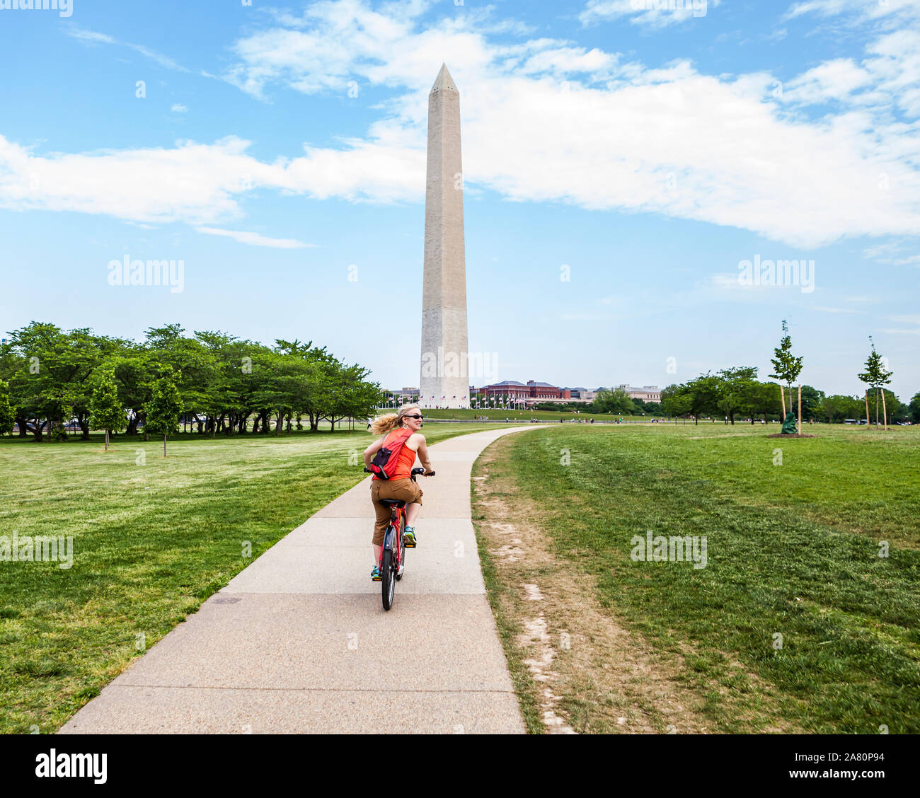 A happy woman riding a bike share bike on the National Mall in Washington D.C., USA. The Washington Monument in the background. Stock Photo