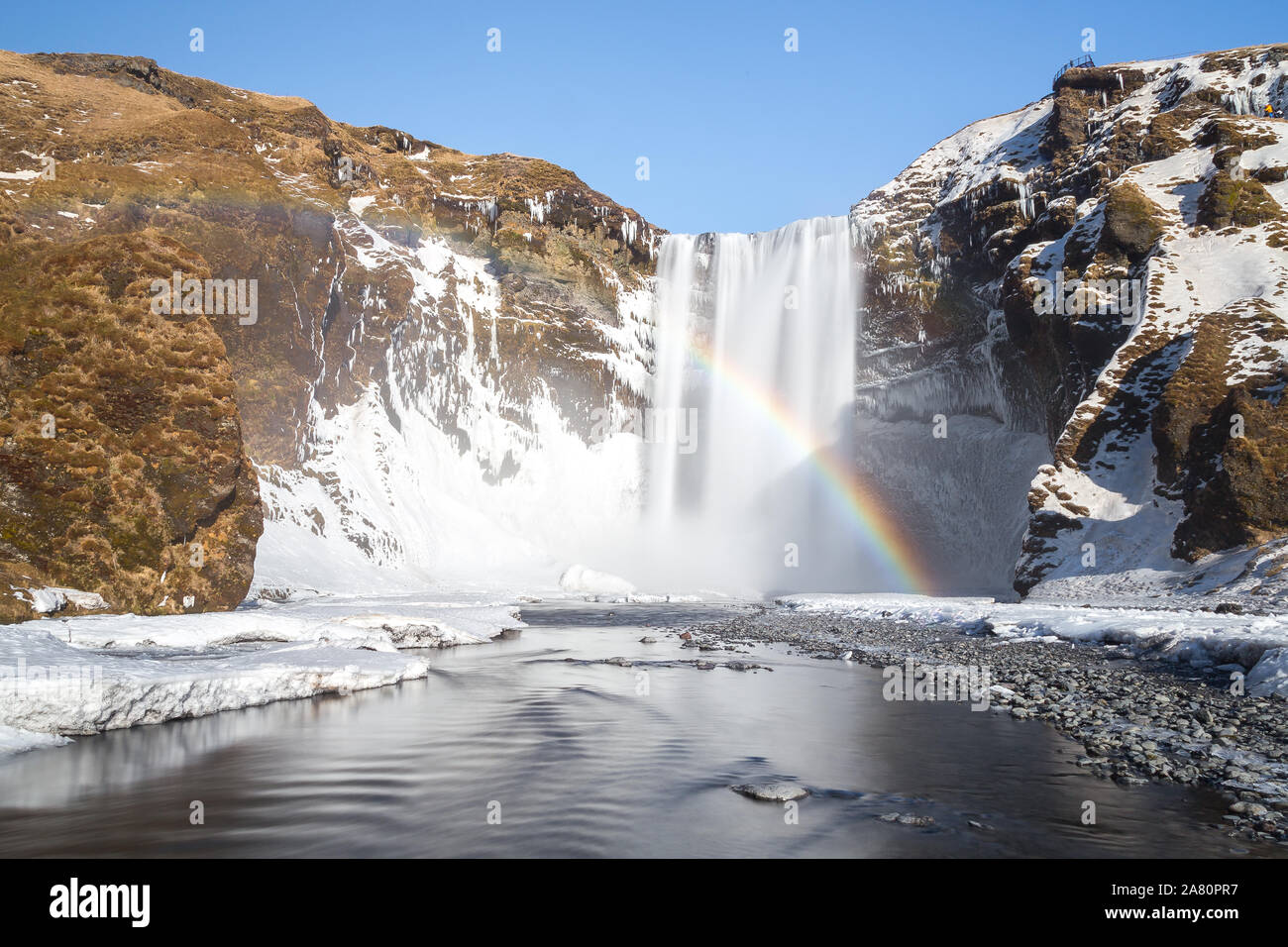 Rainbow in the spray of Skogafoss waterfall, in Iceland. Winter sunny day,  Snowed landscape. Stock Photo