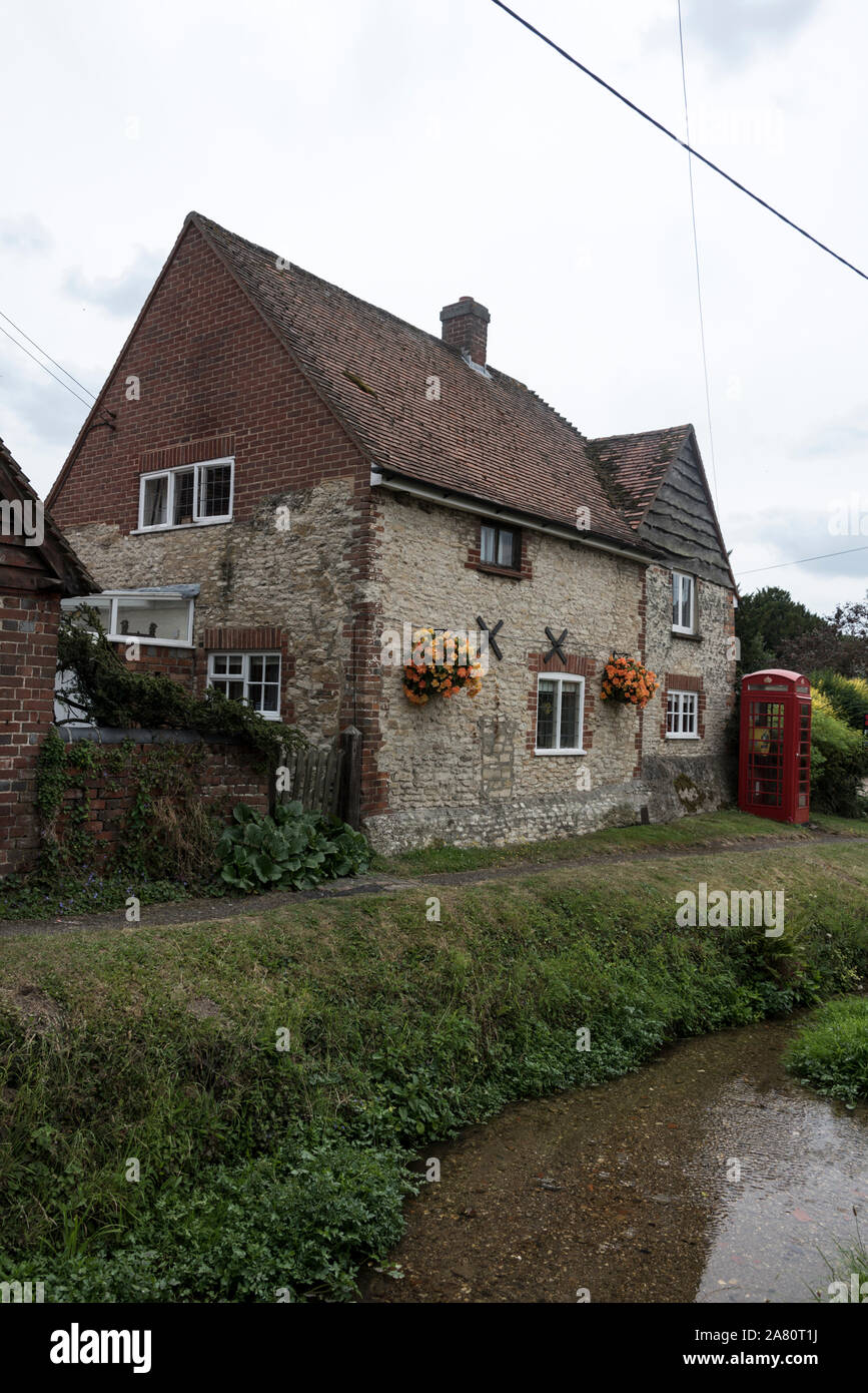 A flint stone built cottage with its floral hanging baskets beside a stream in a small hamlet of Cuxham on the main Watlington- Stadhampton road in ea Stock Photo