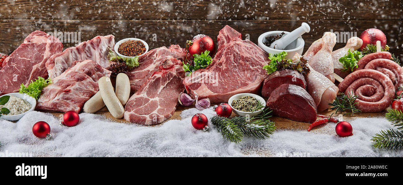 Christmas banner with assorted raw meat for a seasonal winter BBQ displayed on snow with colorful decorations including assorted pork, veal, chicken a Stock Photo