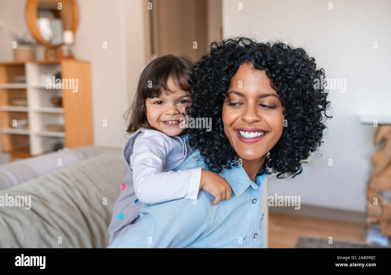 Smiling mom piggybacking her adorable daughter around the house Stock Photo