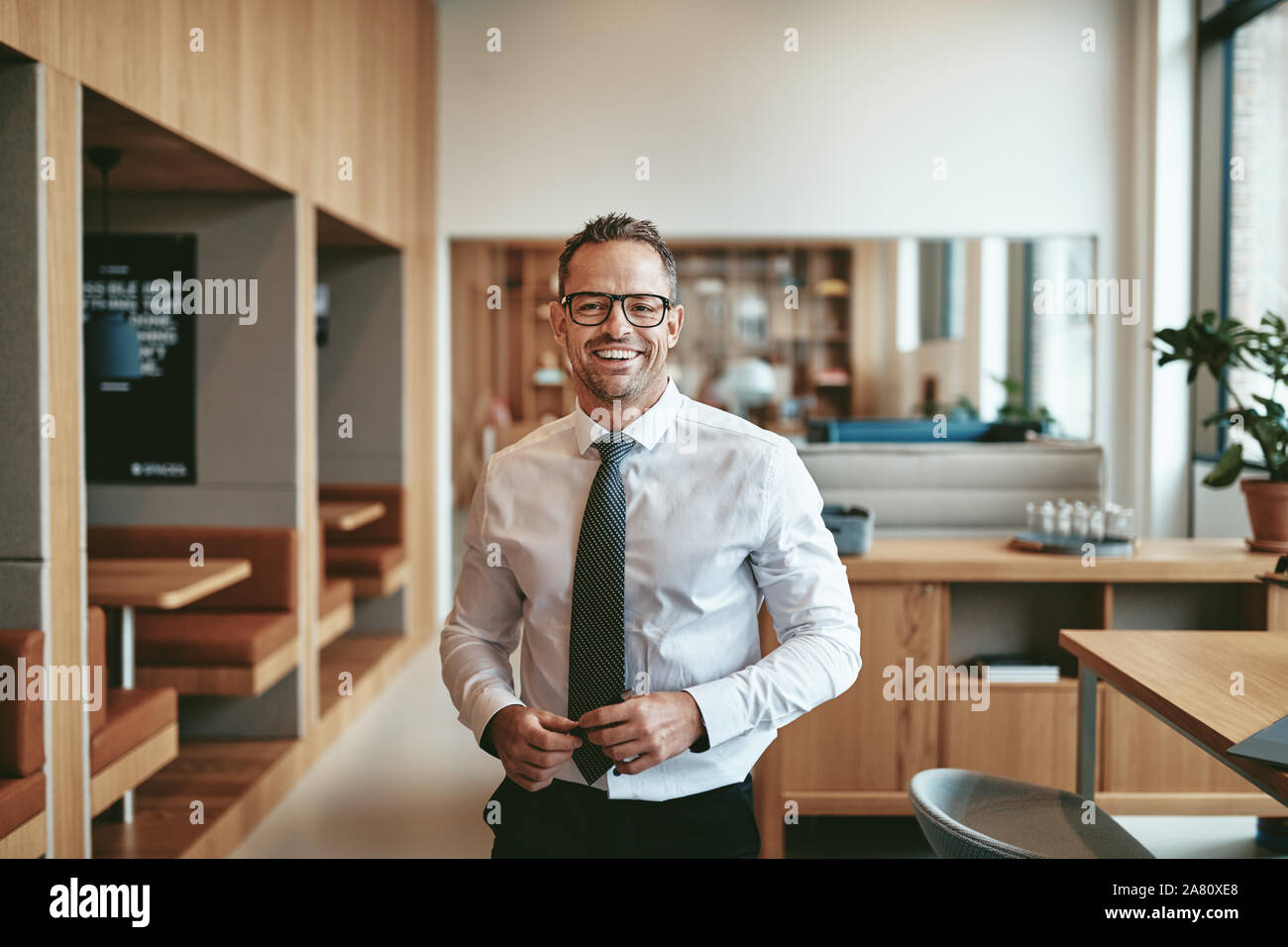 Mature businessman smiling confidently while standing alone in the cafeteria of a bright moderrn office Stock Photo