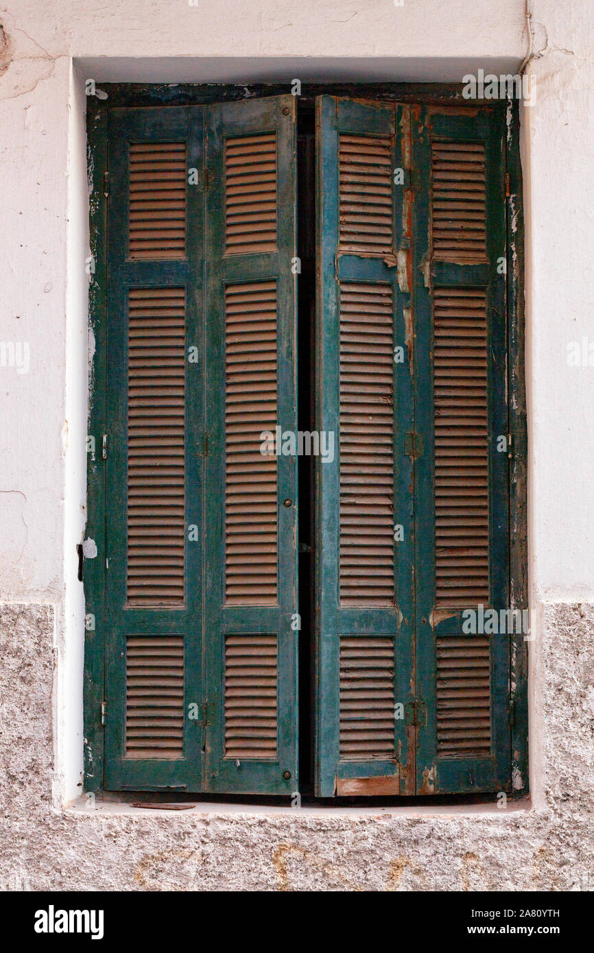 Old green wooden shutters are ajar on the old window against the background of the facade of the house. Stock Photo