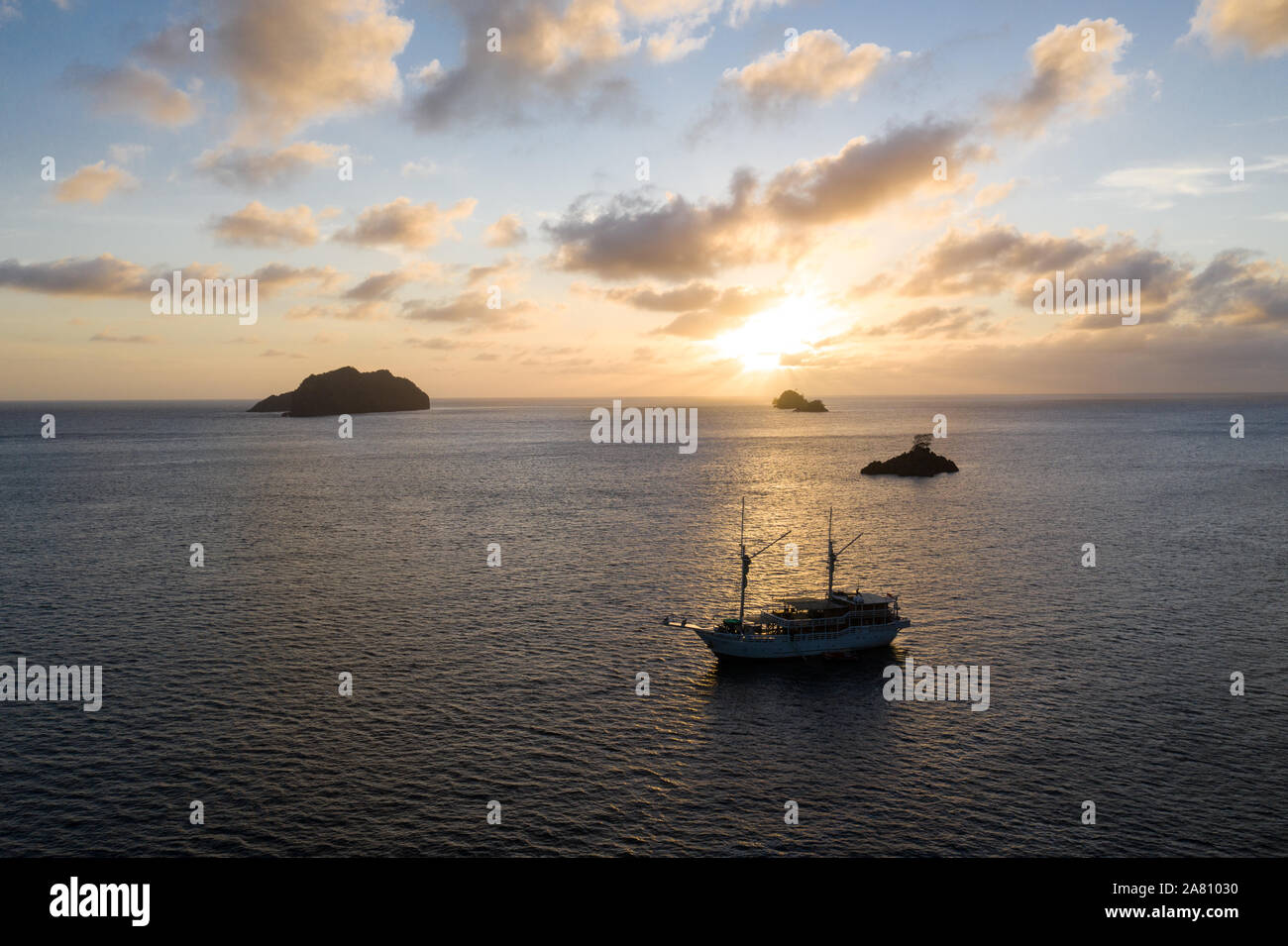 A peaceful sunset silhouettes limestone islands and a Pinisi schooner in Raja Ampat, Indonesia. This area harbors extraordinary marine biodiversity. Stock Photo