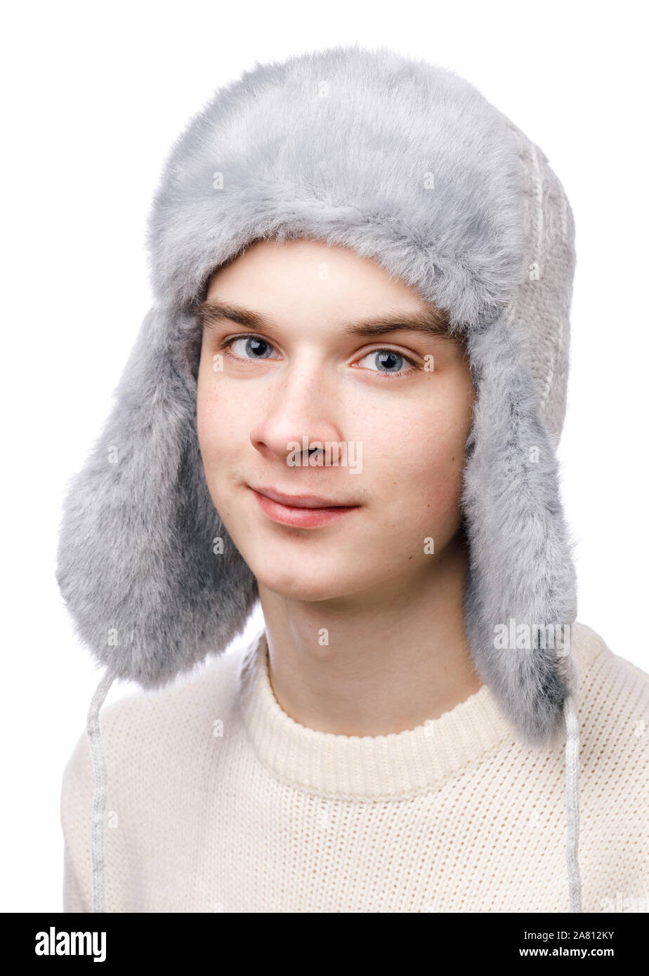 Head and shoulders studio portrait of smiling teenager boy wearing blue knitted faux fur winter trapper hat (Ushanka) and sweater on white background Stock Photo