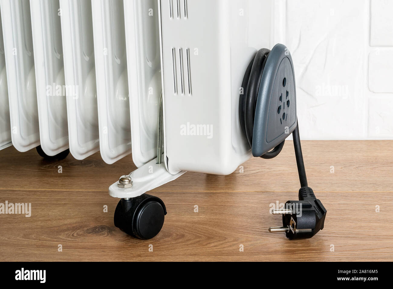 Home electric oil heater on plastic twin wheels and with cable reeled up on  a cable storage. White oil-filled radiator on a brown wooden floor Stock  Photo - Alamy