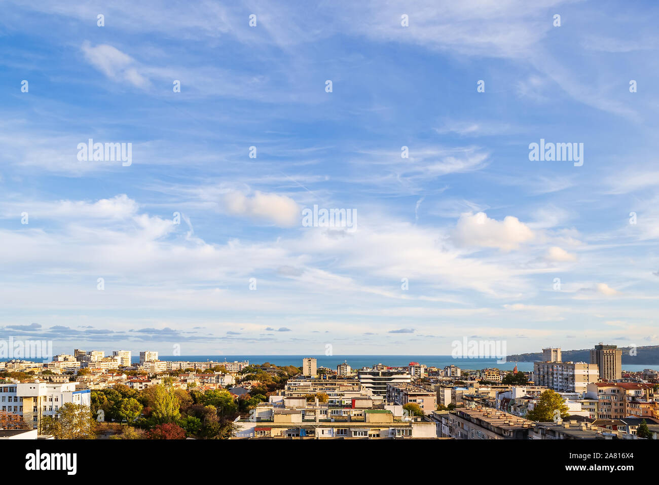 Beautiful blue sky with scenic fluffy clouds over seaside city on a sunny autumn day. Warm tranquil landscape with skyline. Soft focus. Stock Photo