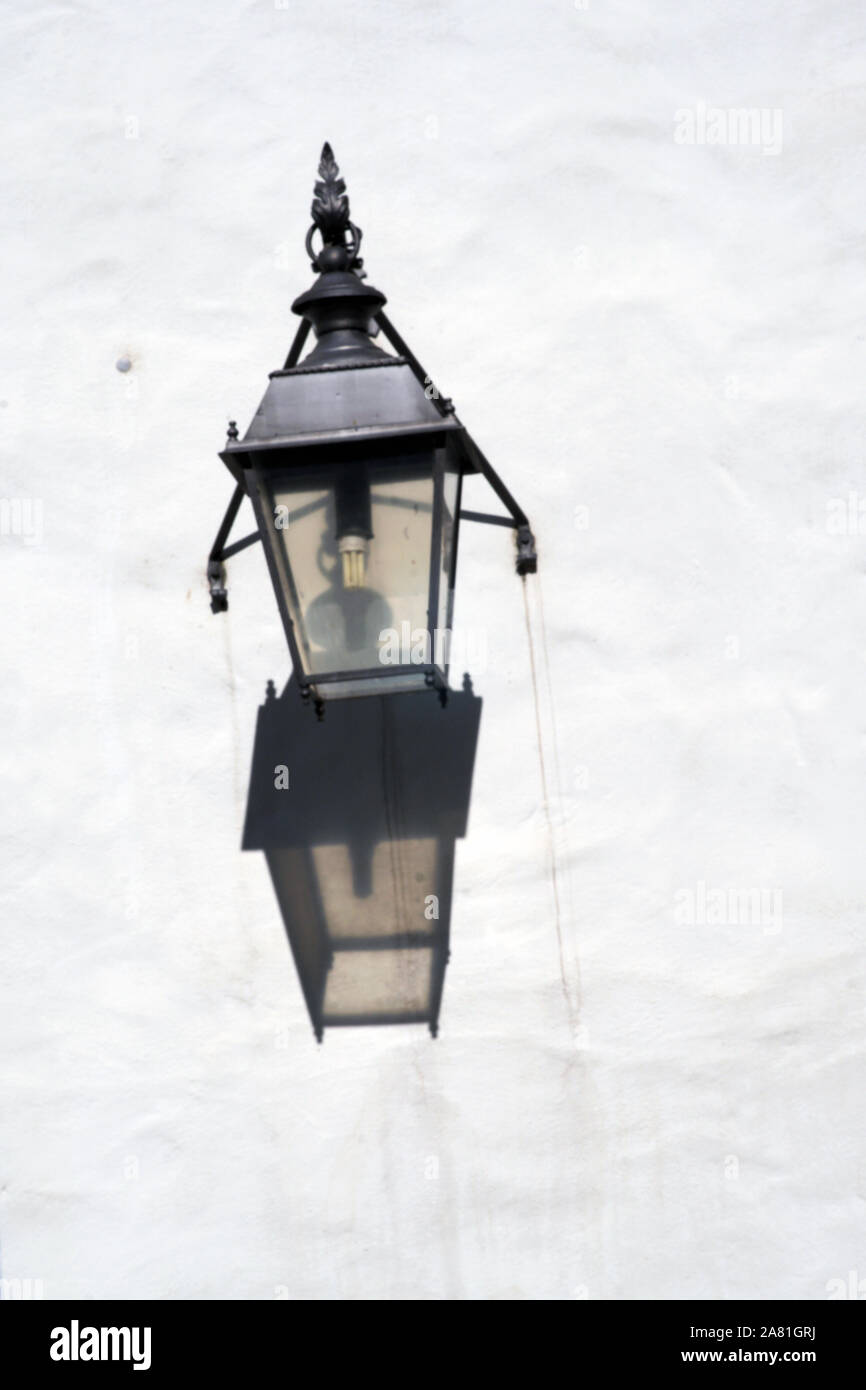 The close-up of a nostalgic wall lamp or lantern casting a shadow on a plaster facade. Stock Photo