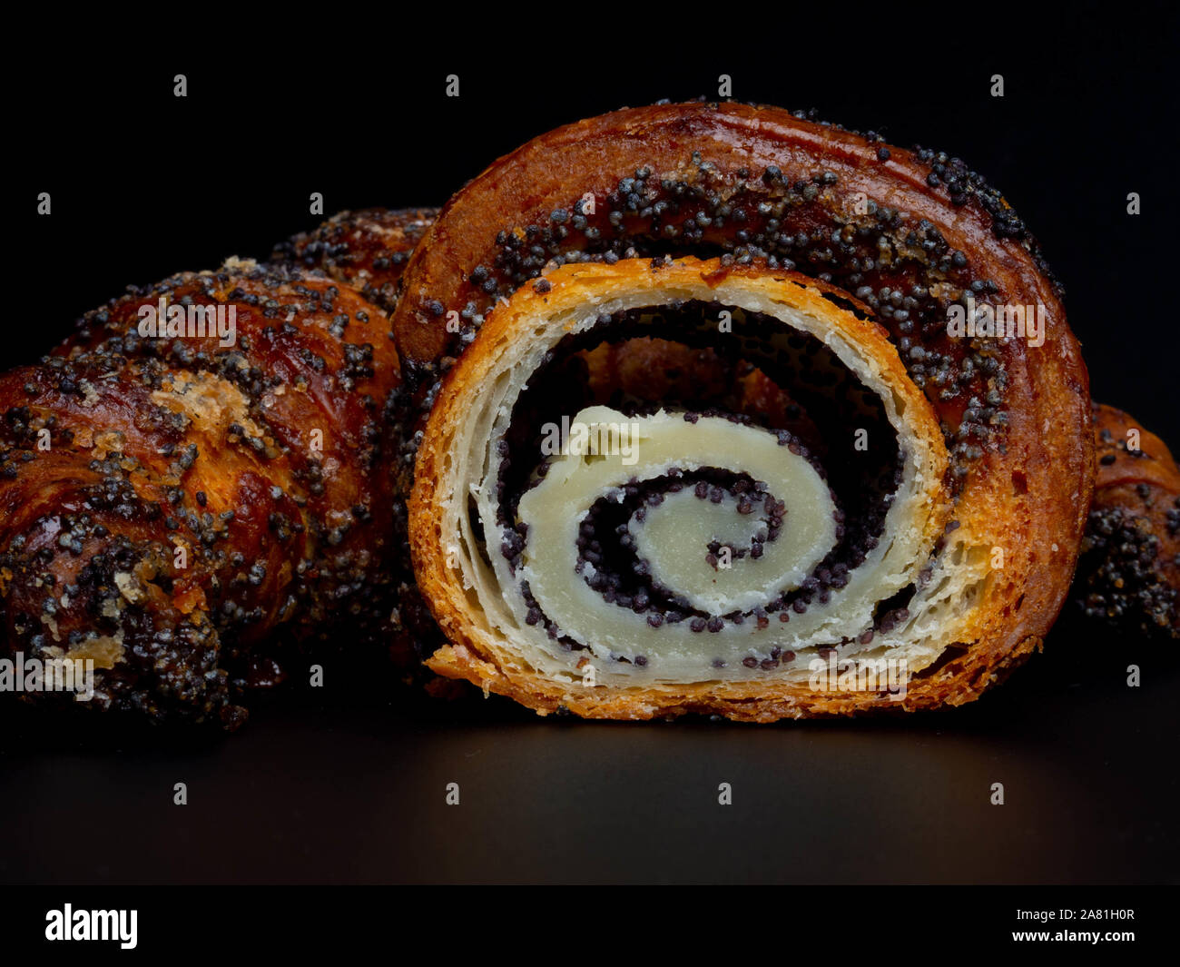 Sweet bun with poppy seeds on black background. Homemade roll horn with